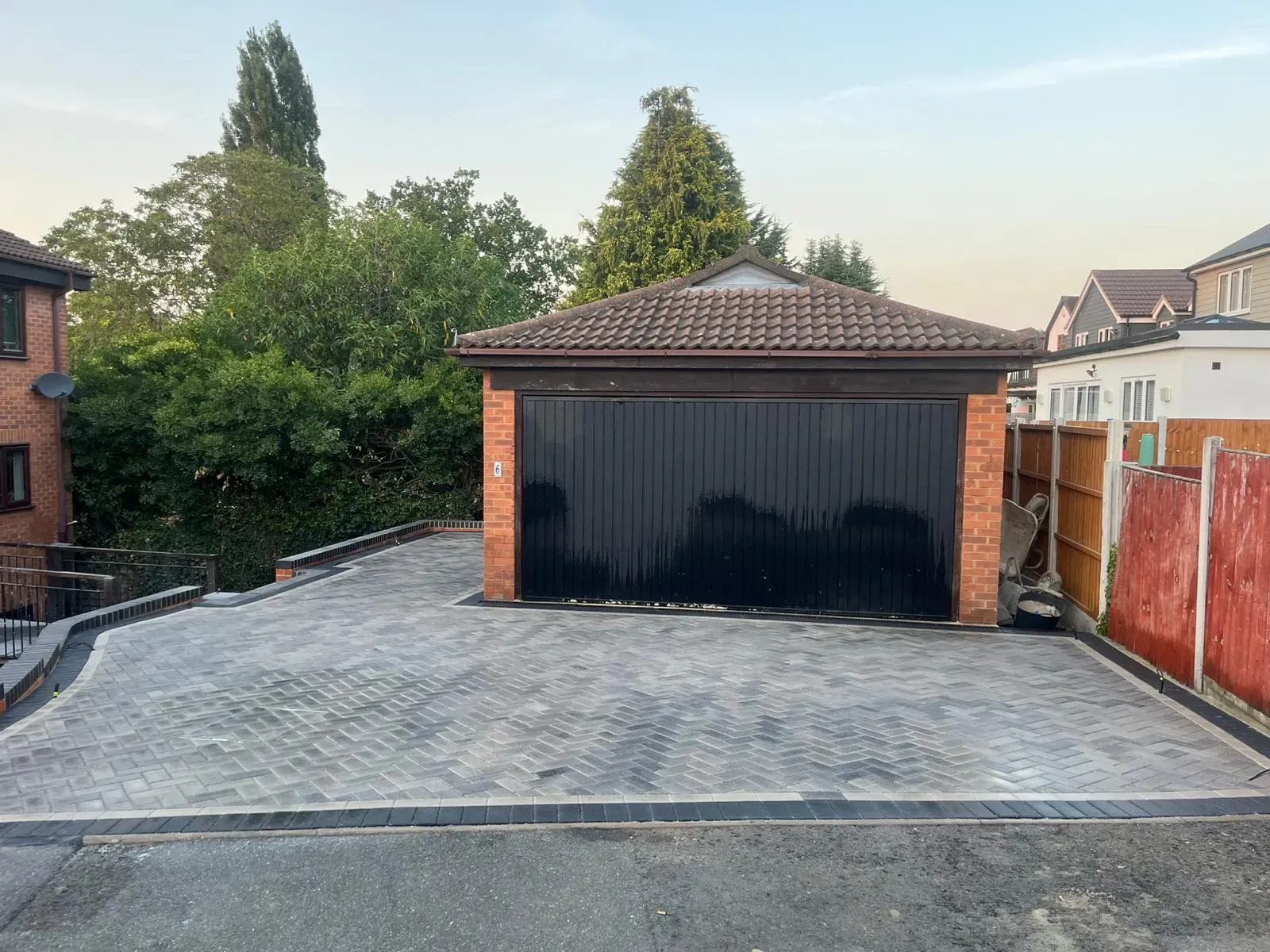 A modern, newly installed block paving driveway in grey and charcoal, with a neat border, leading to a garage with a black door.