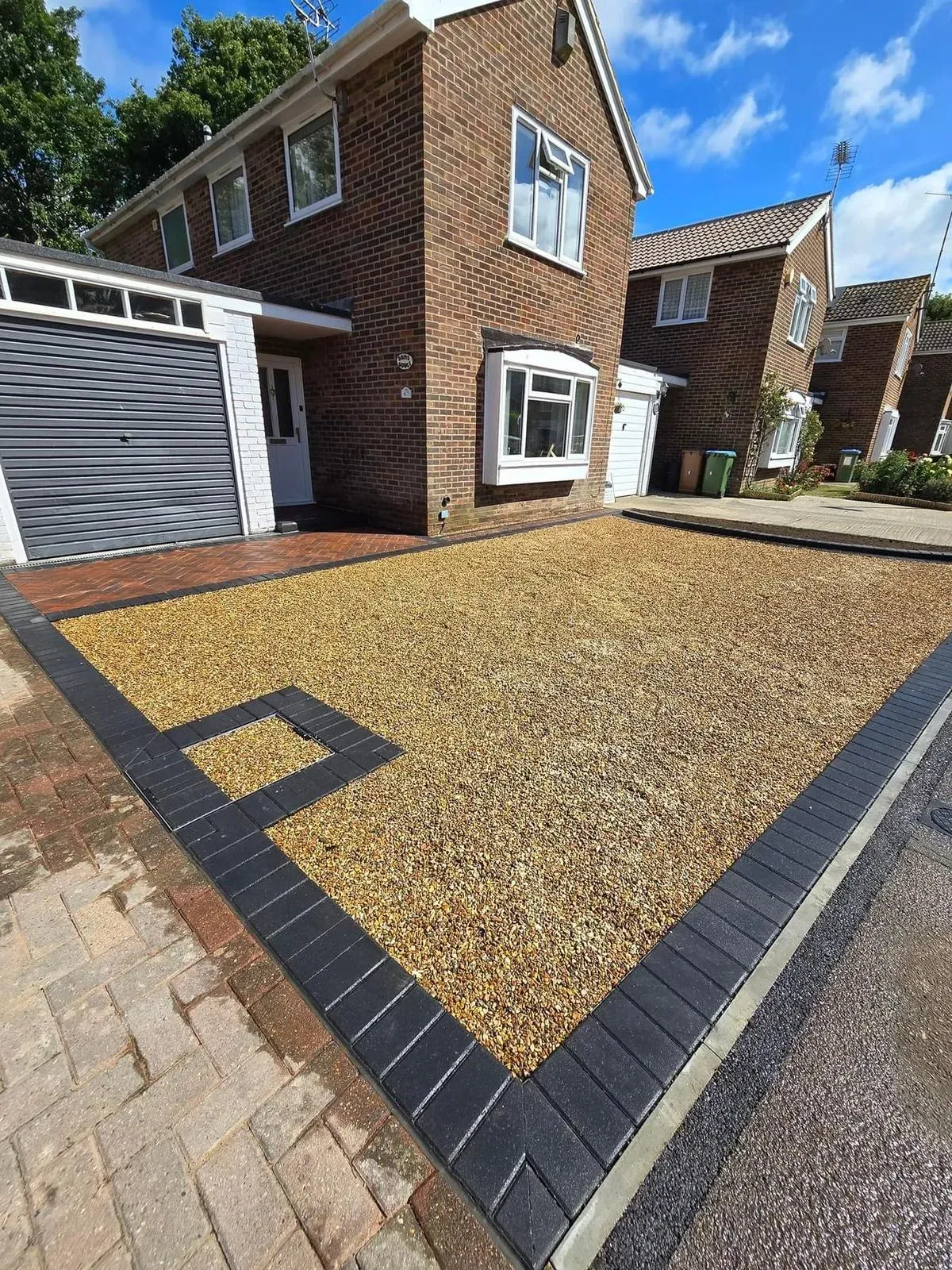 Newly laid gravel driveway with dark block paving edge and integrated drain in front of a modern brick house.