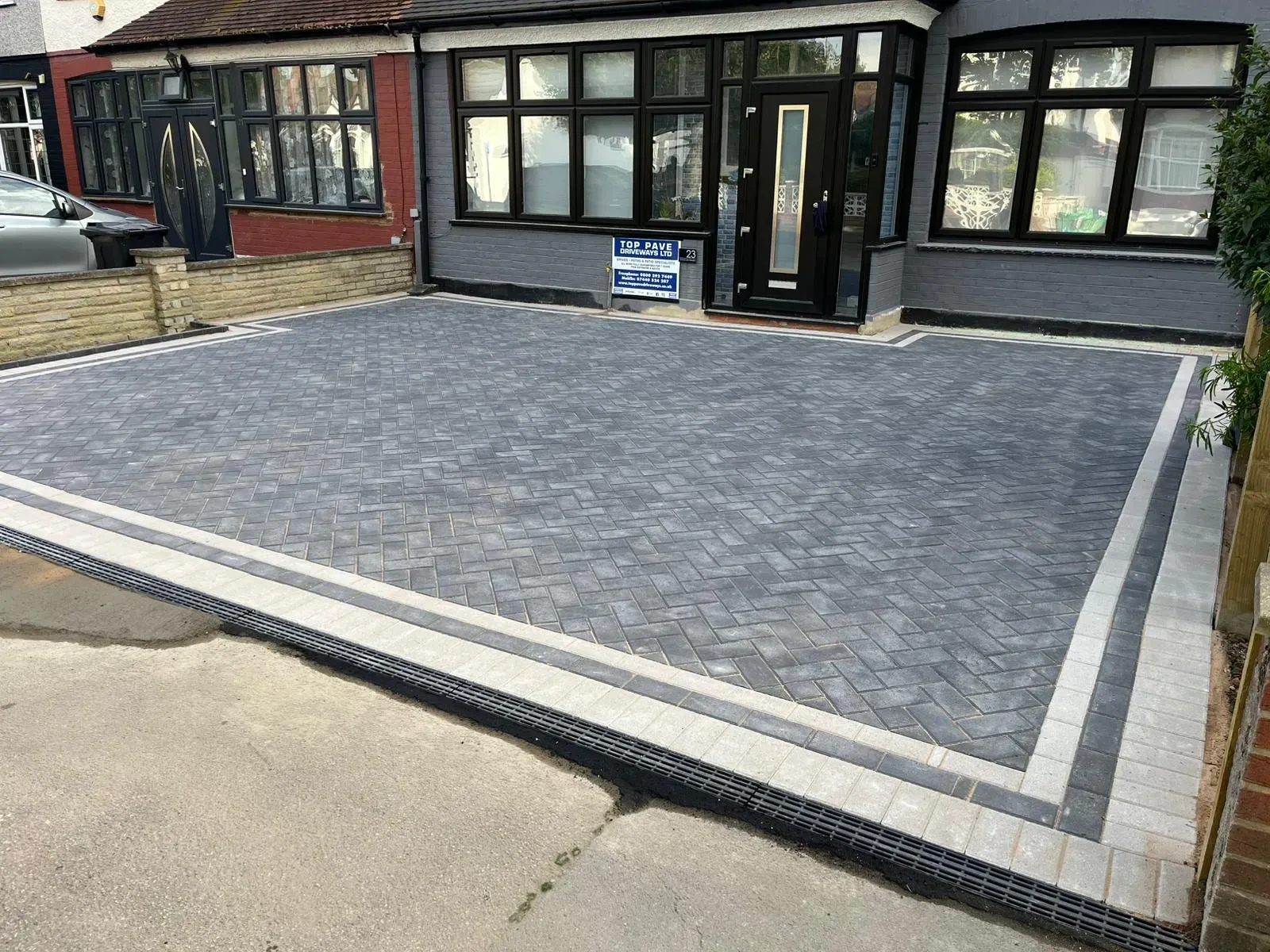 A modern grey block paving driveway with a decorative border and integrated drainage, leading to the entrance of a residential property.