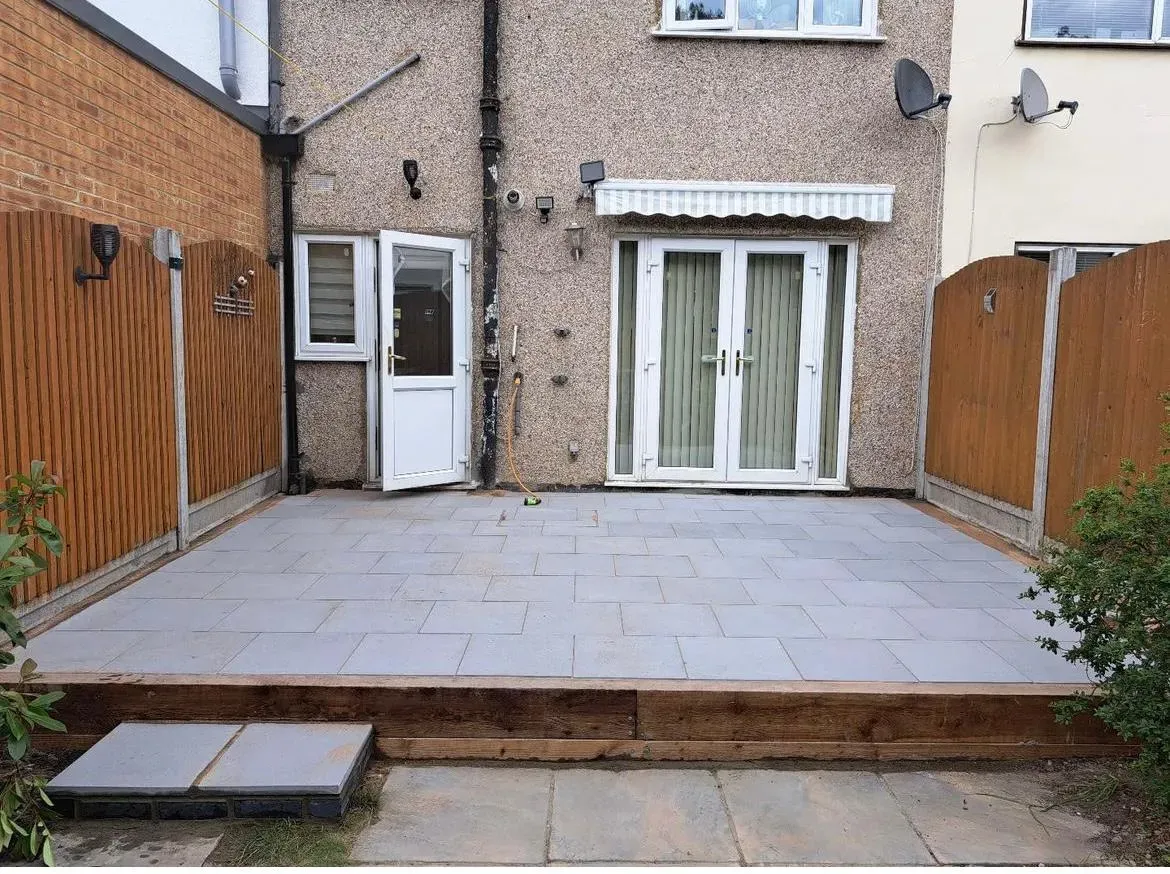A new modern patio with light grey paving slabs and a timber sleeper step in a residential garden.